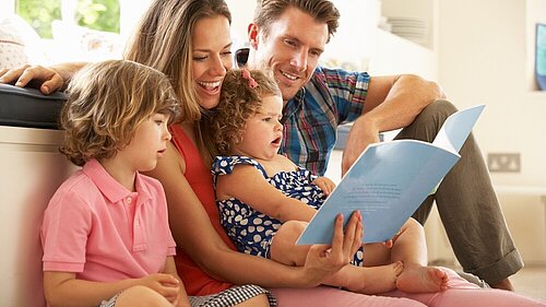 A mother, father, brother and sister sitting reading a book.